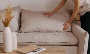 Mani che sistemano un cuscino su un divano beige, un'idea per rivestire divano fai da te.