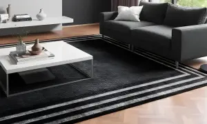 Un elegante soggiorno con un divano grigio e un tavolino bianco. Il pavimento è coperto da un tappeto nero con strisce bianche, perfetto per accostare due tappeti e creare un ambiente moderno.