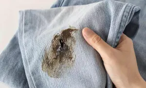 Macchia scura su tessuto di jeans, simile a muffa su tessuti, che rovina il capo.