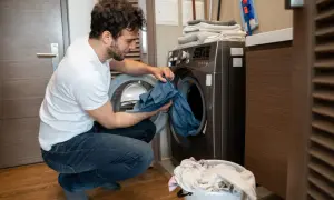 Uomo con maglietta bianca e jeans che carica la lavatrice, preoccupato per come eliminare le macchie da trasferimento di colore blu da un capo.