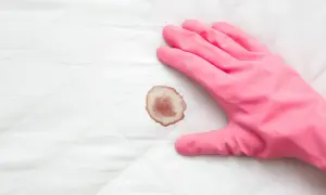 Mano con guanto rosa pronto a pulire macchie di sangue su tessuto bianco trapuntato.