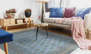 Un soggiorno moderno con un tappeto pakistano blu chiaro, divano beige, cuscini blu e viola, e una coperta rosa.