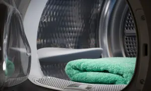 Interno di una lavasciuga con un asciugamano verde piegato. Si vede il cestello metallico e la porta trasparente.