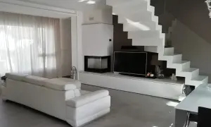 Soggiorno moderno con divano bianco, camino, TV e una scenografica scala a vista bianca. Ottime idee arredare soggiorno con scala a vista.