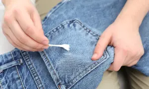 Mani che rimuovono la cingomma dai jeans con un cotton fioc. Ecco come togliere la cingomma dai vestiti.