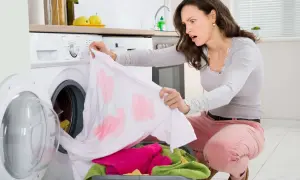 Donna scopre con orrore macchie rosse su un capo bianco appena lavato, un classico problema di come eliminare le macchie da trasferimento di colore rosso.