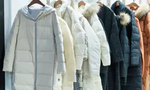 Una fila di piumini color crema, bianchi e neri, alcuni con cappuccio di pelliccia. Se il tuo piumino è bucato, questi rimedi ti aiuteranno a ripararlo.