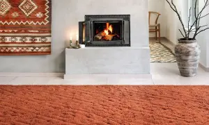 Un tappeto decorativo con motivi geometrici arancioni e bianchi è appeso al muro, un'idea per come appendere un tappeto al muro.