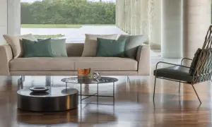 Divano 3 posti beige con cuscini verdi, tavolini rotondi e poltrona di design in un soggiorno moderno.