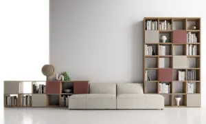 Un comodo divano beige è posizionato davanti a una libreria modulare in legno, piena di libri e oggetti decorativi.