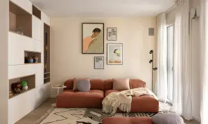 Un accogliente soggiorno con un divano color terracotta e un tappeto su parquet chiaro. Decorazioni alle pareti e una libreria a muro completano l'ambiente.