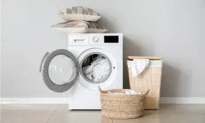 Lavatrice con cestello aperto, cuscini impilati sopra e cesti per la biancheria. Pronto per scoprire come lavare le tovaglie in lavatrice.