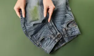 Mani che indicano una macchia verde su jeans, per mostrare come togliere macchie di jeans su ecopelle.