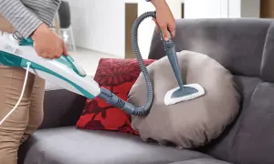 Come togliere macchie dal divano con un pulitore a vapore. La persona pulisce un cuscino del divano con un accessorio a spazzola.
