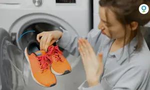 Donna con scarpe arancioni vicino a una lavatrice, con espressione disgustata. Scopri come profumare la lavatrice per un bucato fresco.