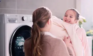 Bambina felice abbraccia maglione morbido, vicino a una lavatrice LG con funzione allergy care.