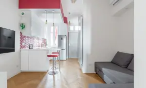 Un accogliente open space di 20 mq con cucina moderna, divano grigio e dettagli rossi vivaci.