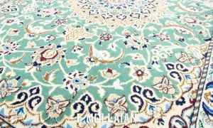 Un raffinato tappeto persiano verde, con intricati motivi floreali e un bordo decorato, evoca un'eleganza senza tempo.