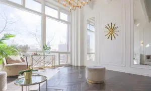 Un elegante soggiorno con un tavolino rotondo dorato, un pouf beige e un orologio a muro dorato a forma di sole.