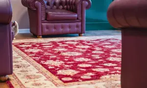 Un tappeto Yalameh rosso con motivi floreali chiari, adagiato su un pavimento in legno, accanto a poltrone in pelle bordeaux.
