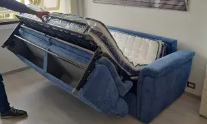 Apertura divano letto: un braccio solleva il meccanismo interno, rivelando il materasso ancora imballato.
