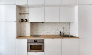 Moderna cucina bianca con paraschizzi a esagoni geometrici, piano in legno e forno in acciaio.