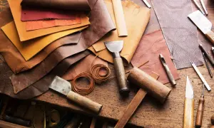 Pelle, colori e attrezzi da artigiano. Un tavolo da lavoro con vari tipi di pelle, strumenti per lavorarla come punzoni, coltelli e martelli.