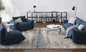 Un ampio tappeto 3 metri con motivi astratti grigi e blu, che completa un salotto moderno con divani blu e tavolino bianco.