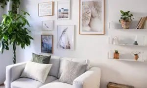 Galleria di quadri e mensole bianche sopra un divano bianco, con piante e oggetti decorativi. Idee mensole sopra divano per un tocco di stile.