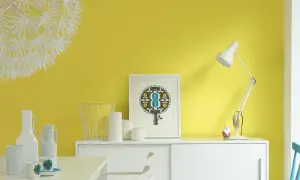 Parete giallo dorato illumina un mobile bianco con vasi, una lampada e un quadro. Un piccolo gnomo sorveglia la scena.
