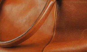 Dettaglio di una borsa in pelle marrone, con la texture del materiale che mostra lievi graffi sulla pelle, testimoni di un uso vissuto.