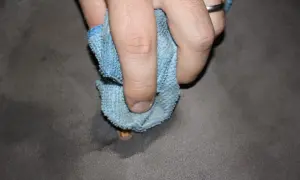 Mano che pulisce una bruciatura da sigaretta su tessuto grigio con un panno blu.