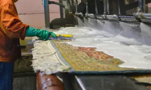 Un operaio lava un tappeto persiano con una spazzola, sotto getti d'acqua e schiuma. Il costo del lavaggio tappeto persiano è un investimento per preservarne la bellezza.