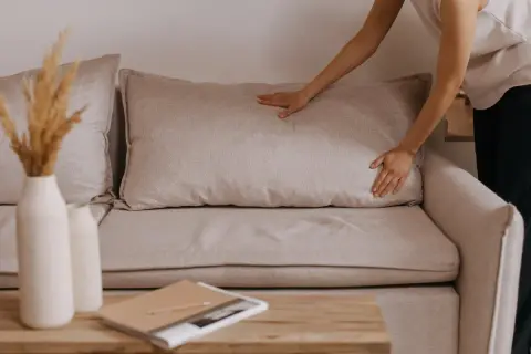 Mani che sistemano un cuscino su un divano beige, un'idea per rivestire divano fai da te.