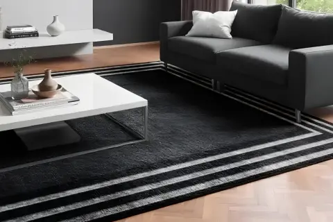 Un elegante soggiorno con un divano grigio e un tavolino bianco. Il pavimento è coperto da un tappeto nero con strisce bianche, perfetto per accostare due tappeti e creare un ambiente moderno.