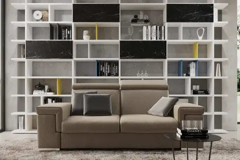 Divano moderno in un soggiorno ampio, con libreria bianca a giorno piena di libri e oggetti d'arte.