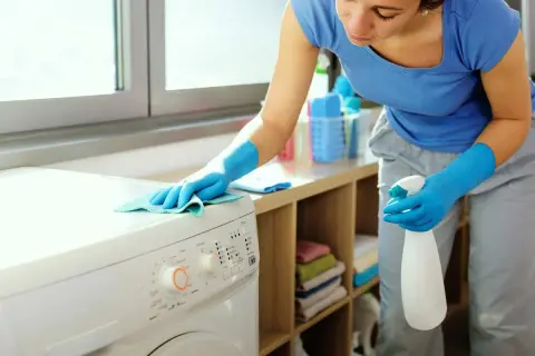 Donna con guanti blu pulisce la lavatrice. Effettua il primo lavaggio lavatrice a vuoto per igienizzarla.