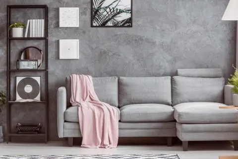 Un divano grigio con coperta rosa, libreria nera con piante e vinile, e un tavolino di legno: idee su cosa mettere vicino al divano per un tocco moderno.
