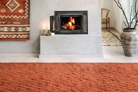 Un tappeto decorativo con motivi geometrici arancioni e bianchi è appeso al muro, un'idea per come appendere un tappeto al muro.