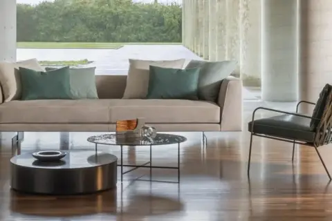 Divano 3 posti beige con cuscini verdi, tavolini rotondi e poltrona di design in un soggiorno moderno.