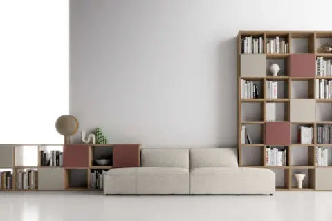 Un comodo divano beige è posizionato davanti a una libreria modulare in legno, piena di libri e oggetti decorativi.