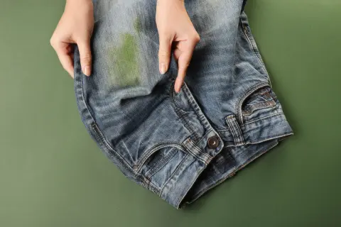 Mani che indicano una macchia verde su jeans, per mostrare come togliere macchie di jeans su ecopelle.