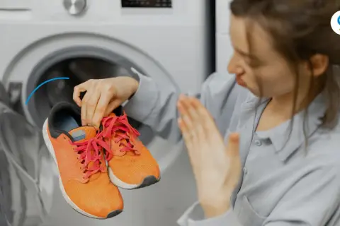 Donna con scarpe arancioni vicino a una lavatrice, con espressione disgustata. Scopri come profumare la lavatrice per un bucato fresco.