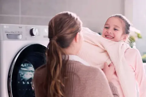 Bambina felice abbraccia maglione morbido, vicino a una lavatrice LG con funzione allergy care.