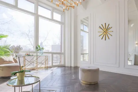 Un elegante soggiorno con un tavolino rotondo dorato, un pouf beige e un orologio a muro dorato a forma di sole.