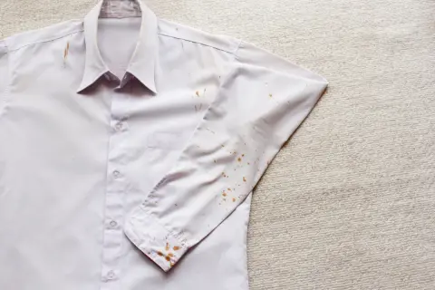 Camicia bianca con macchie di ruggine vecchie sui tessuti, soprattutto sulla manica e sul colletto.