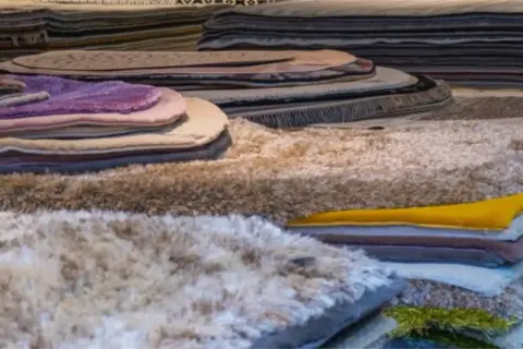 Pile di tappeti morbidi e colorati, tra cui un tappeto seta che brilla.
