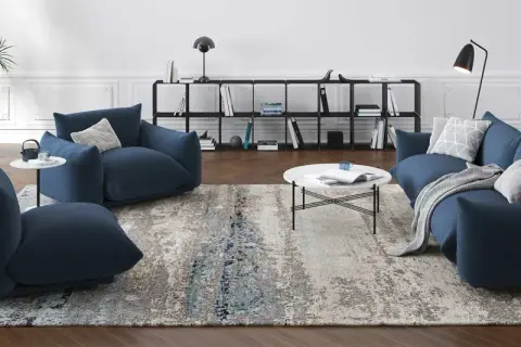 Un ampio tappeto 3 metri con motivi astratti grigi e blu, che completa un salotto moderno con divani blu e tavolino bianco.