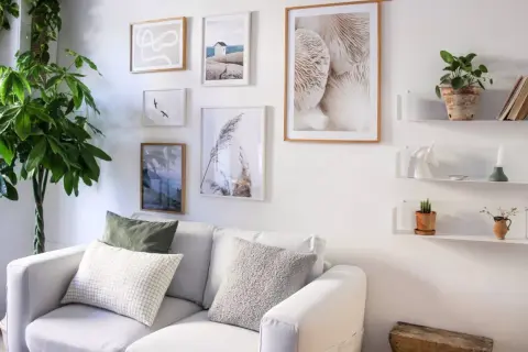 Galleria di quadri e mensole bianche sopra un divano bianco, con piante e oggetti decorativi. Idee mensole sopra divano per un tocco di stile.