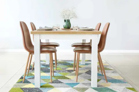 Tappeto sotto il tavolo da pranzo: sì! Un tappeto geometrico colorato aggiunge stile e comfort alla zona pranzo con sedie in pelle marrone.